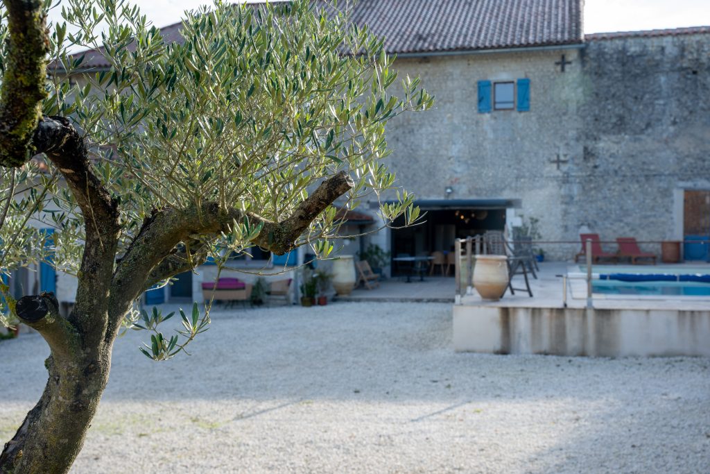 Façade extérieure en pierre du gîte et de la Chambre d'Hôte Le Patio Bleu près d’Aubeterre en Charente, avec volets bleus et cour en gravier