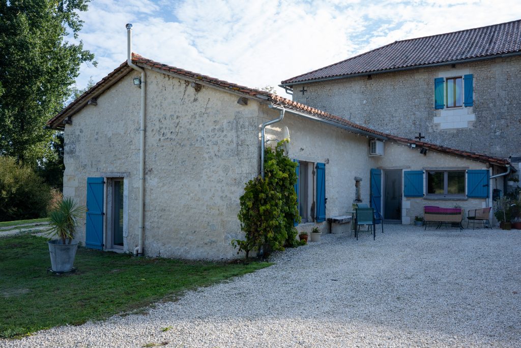 Façade extérieure en pierre du gîte Le Patio Bleu près d’Aubeterre en Charente, avec volets bleus et cour en gravier