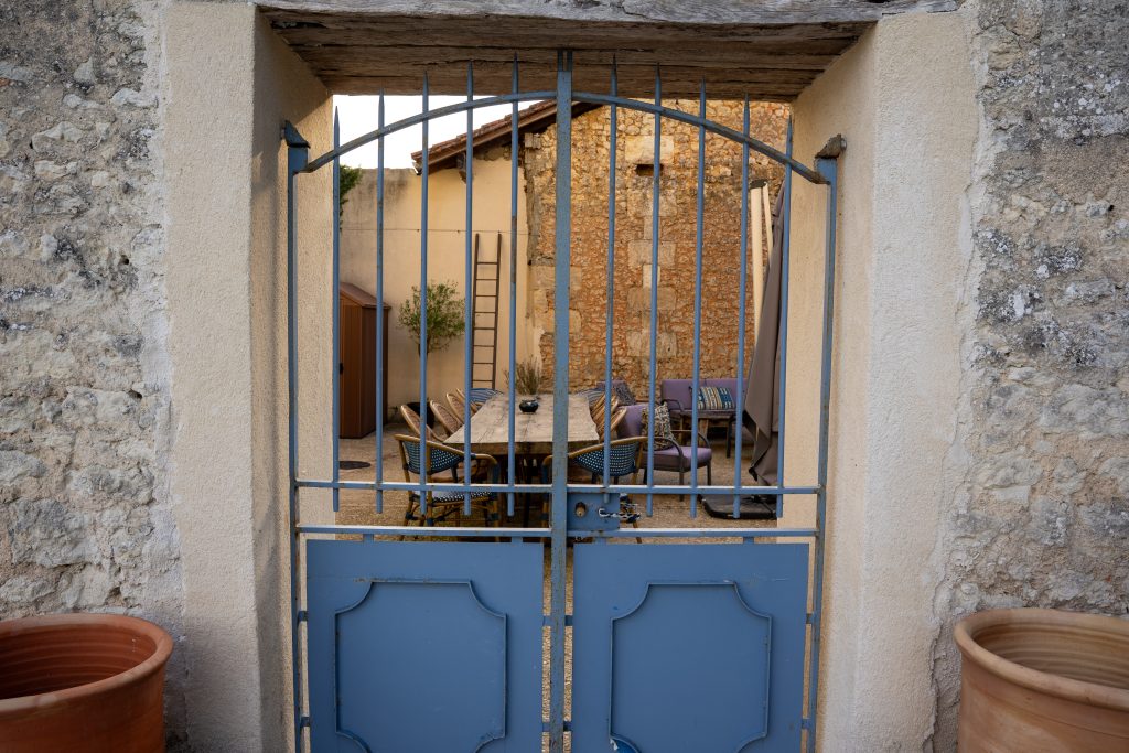 Vue à travers le portail bleu sur la terrasse extérieure du Patio Bleu près d’Aubeterre en Charente, espace partagé entre le gîte et la maison d’hôtes avec grande table conviviale