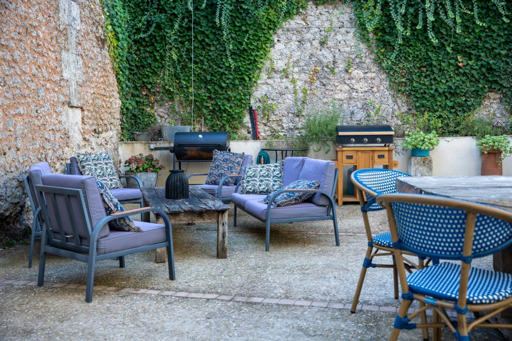 Terrasse conviviale de la maison d’hôtes et du gite Le Patio Bleu près d’Aubeterre en Charente, avec salon de jardin, barbecue et murs en pierre couverts de lierre