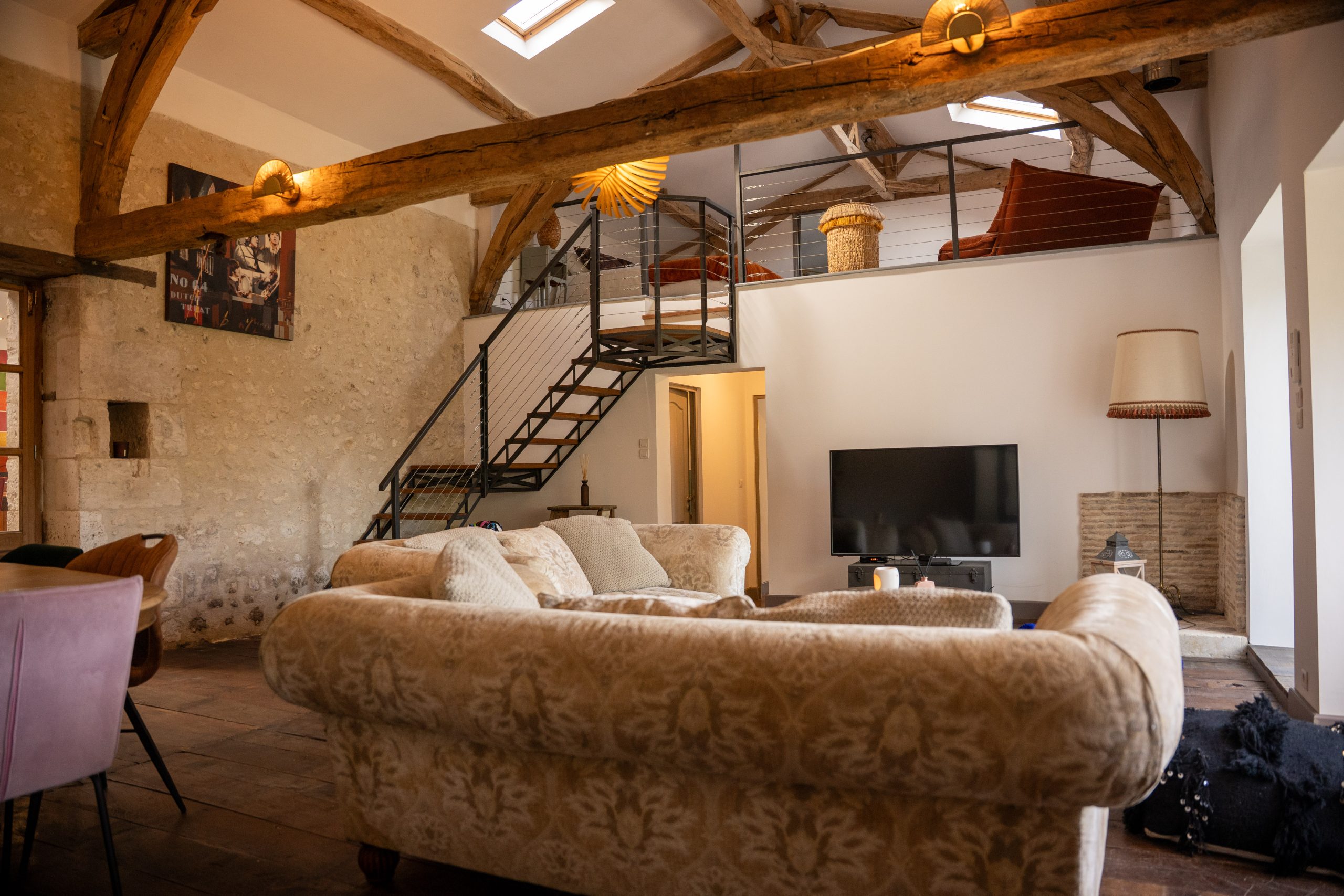 Grand salon du gîte Le Patio Bleu près d’Aubeterre en Charente, avec poutres apparentes, canapés confortables, mezzanine et télévision