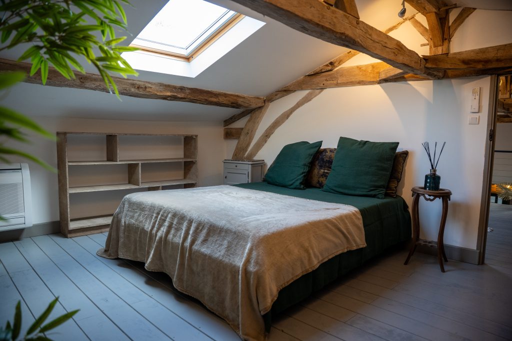 Chambre mansardée du gîte Le Patio Bleu près d’Aubeterre en Charente, avec poutres apparentes, lit double et fenêtre de toit apportant lumière naturelle